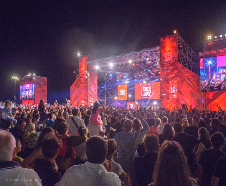 Excited crowd at an outdoor summer concert, vibrant lights, electrifying atmosphere.