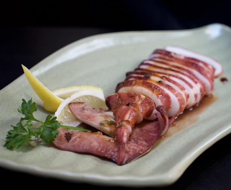 Grilled squid on a plate, garnished with lemon and parsley, deliciously inviting.