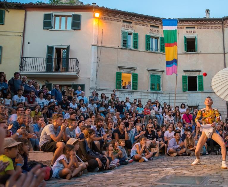 Street performers captivate the crowd with umbrellas and acrobatics in a bustling square.