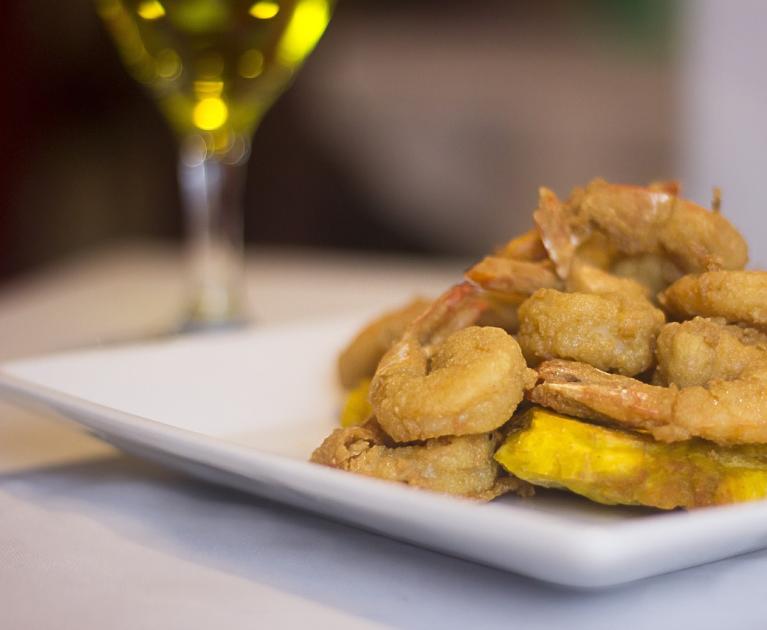 Crispy fried shrimp on a white plate, paired with a glass of wine.