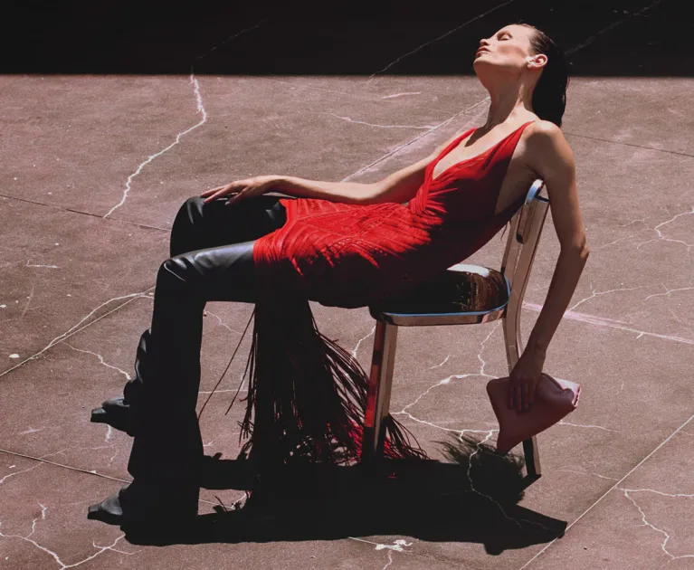 Woman in red, elegant pose under the sun on cracked pavement.