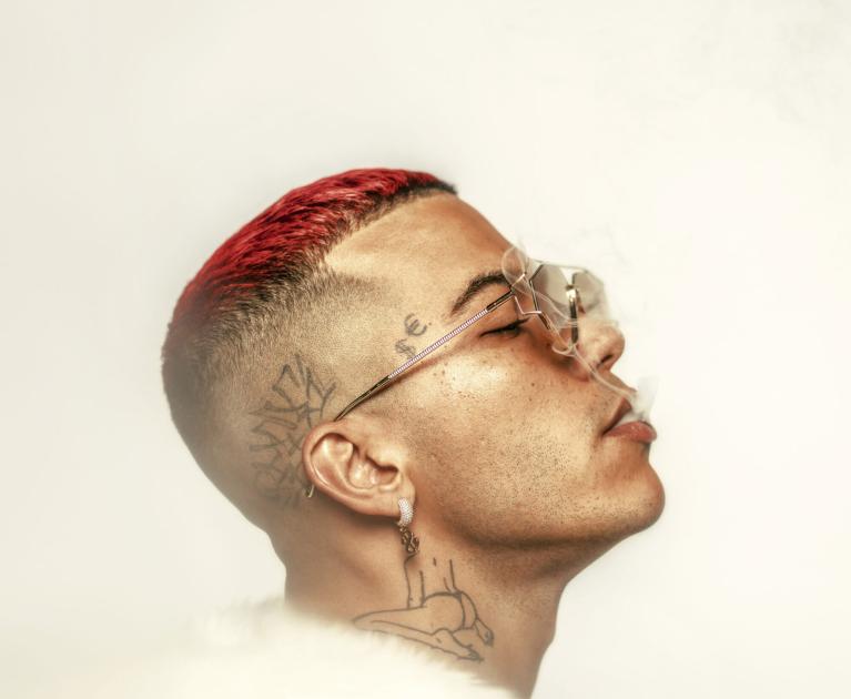 Man with red hair, glasses, tattoos, and smoke, exudes style and rebellion.