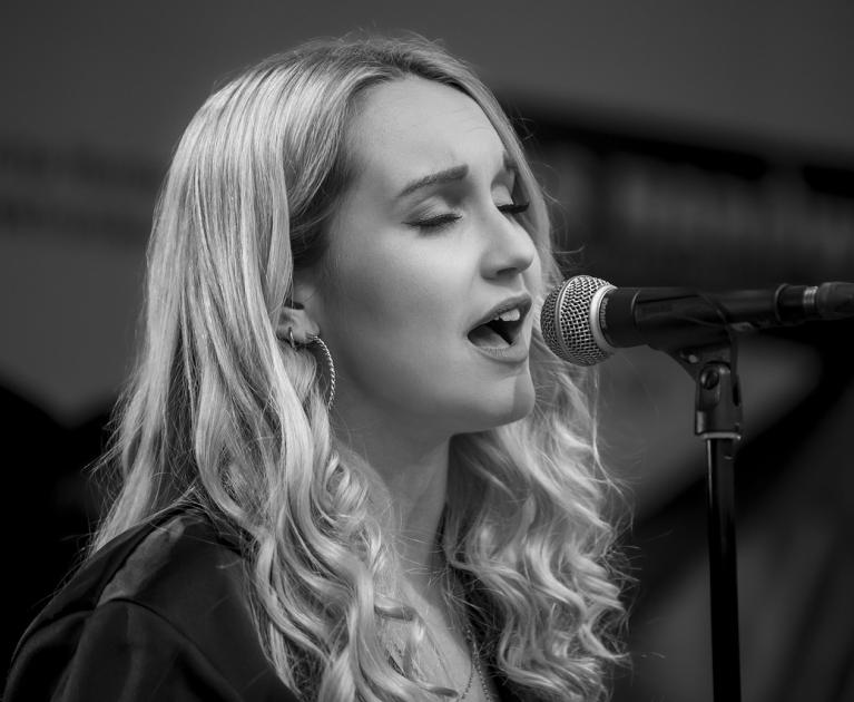 Emotional singer passionately sings into microphone, eyes closed, wavy hair flowing.