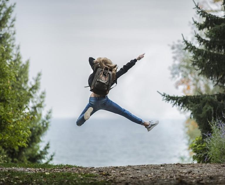 Person jumps joyfully on a natural path, backpack and freedom.