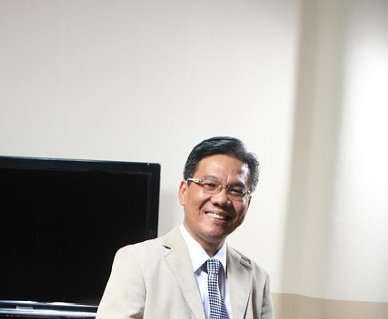 Smiling man in light jacket, seated with tablet, professional atmosphere.