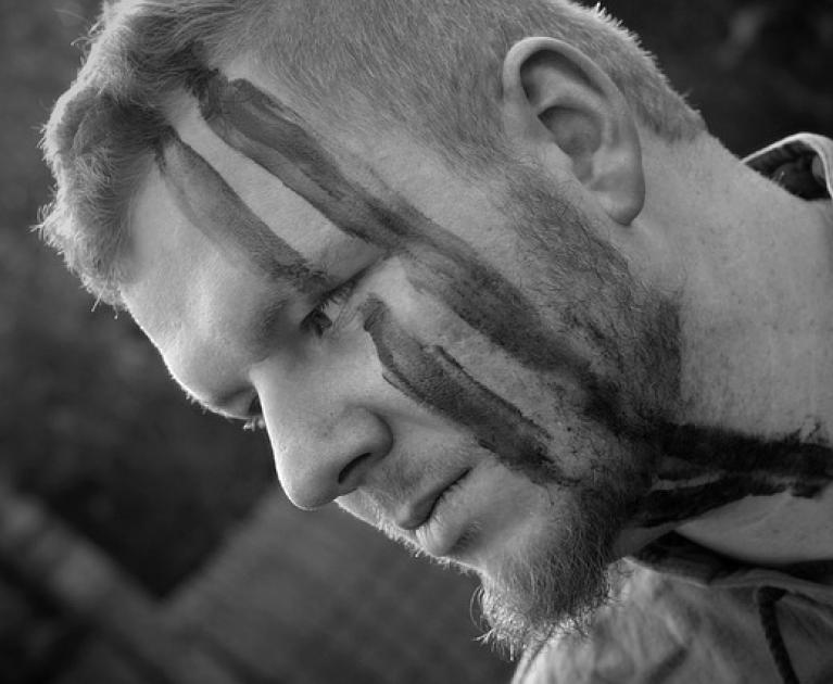 Serious man with face paint marks, intense and contemplative atmosphere.