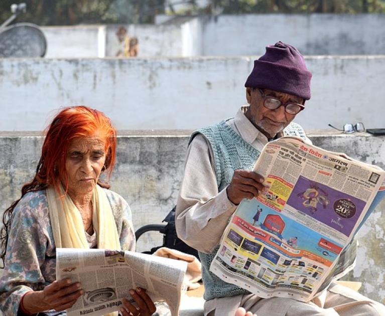 Two elderly people read newspapers outdoors, immersed in morning tranquility.